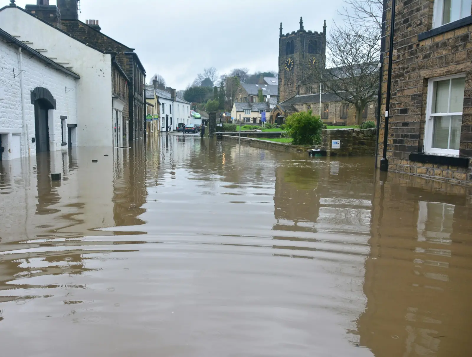 A town street of stone buildings with brown floodwater filling the road
