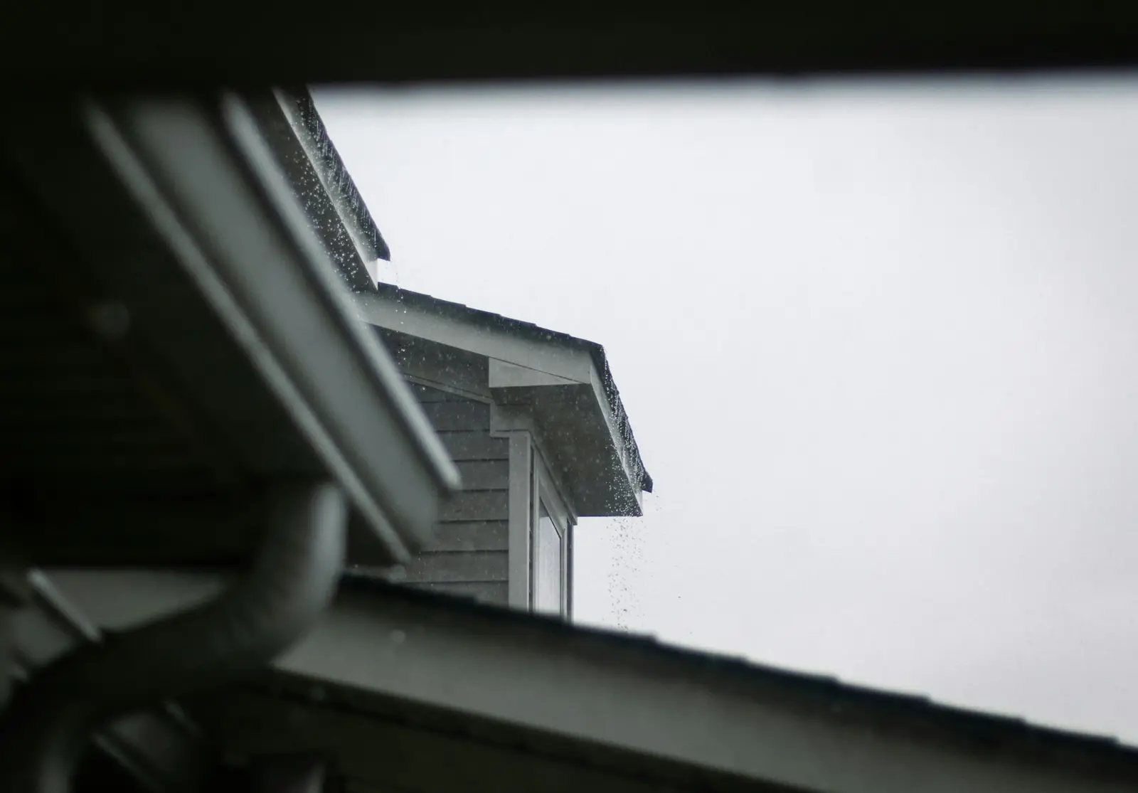 A roof gutter and downspout on a house on a grey, rainy day