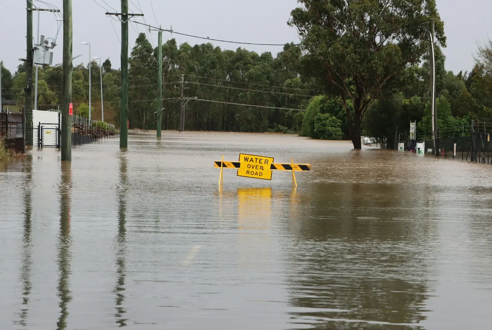 A yellow Water Over Road sign standing in floodwater that covers a road
